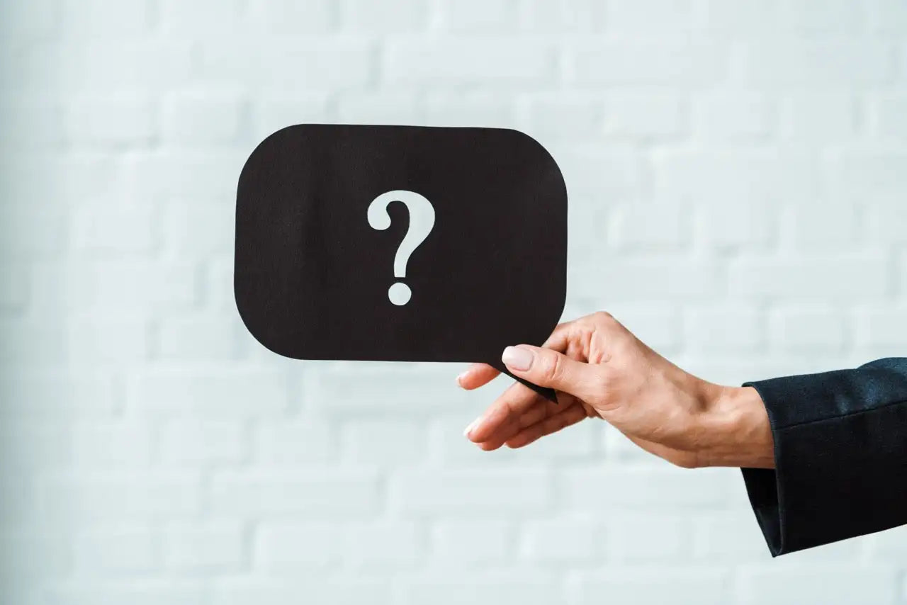 Black rectangular speech bubble with a white question mark, held by a hand in a dark suit sleeve.
