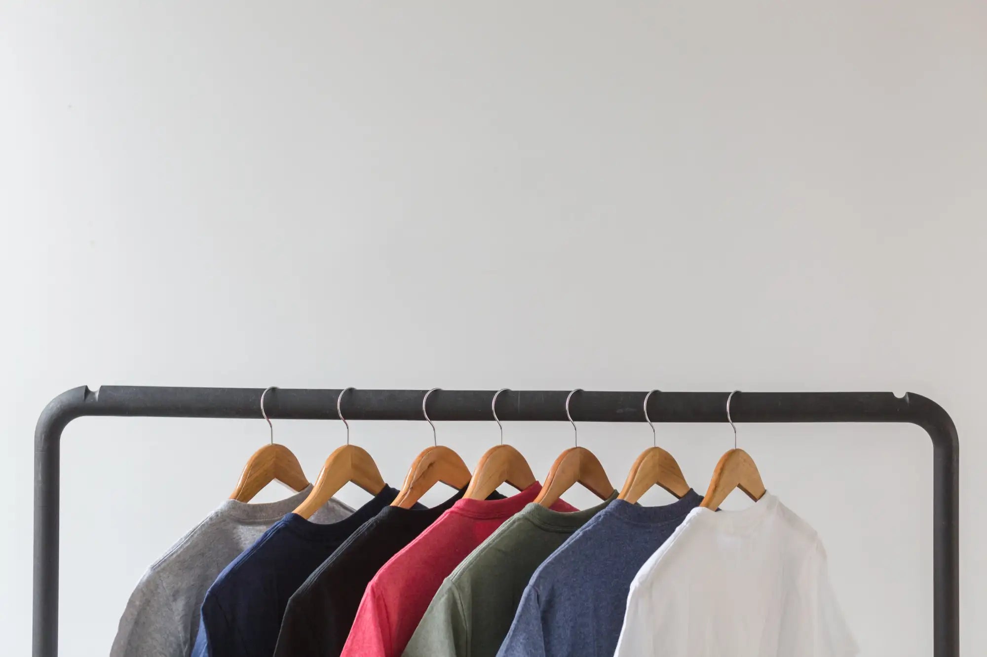 A row of colorful, plain cotton t-shirts hanging neatly on wooden hangers.